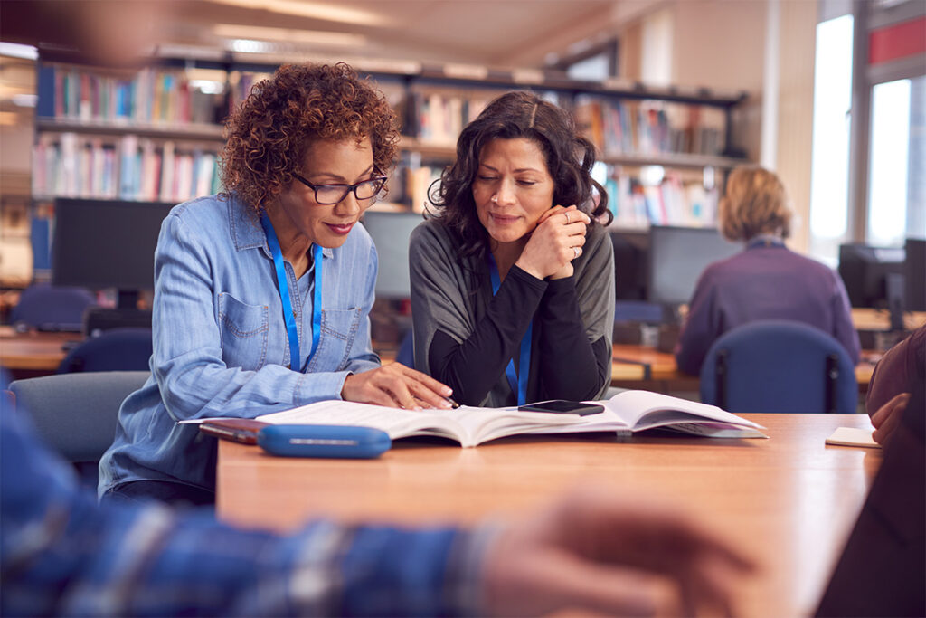 Two women reading a textbook in a library