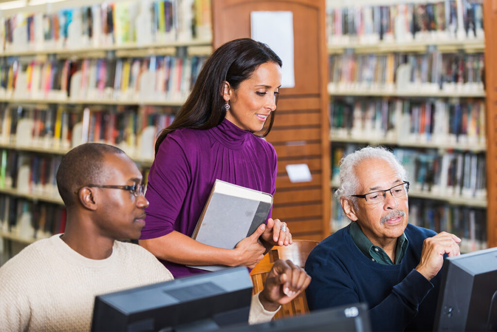 Librarian talking to two people using computers in a library