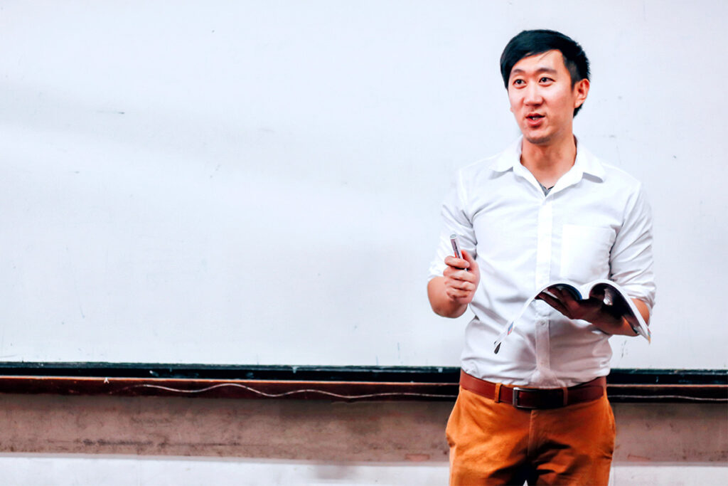 Man holding a book and talking at the front of a classroom