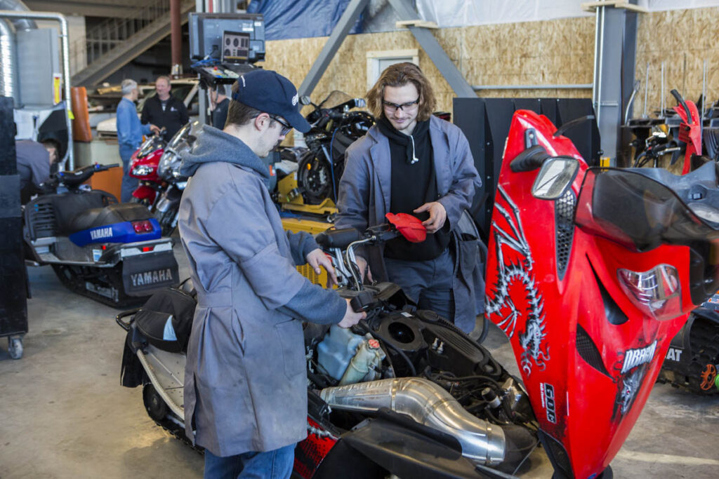 Students in a garage looking at a snowmobile