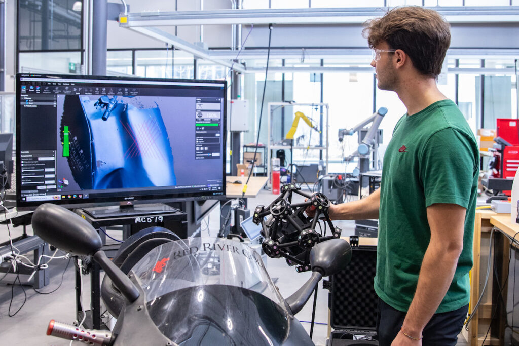 Student using a 3D scanner on a motorcycle in a shop environment.