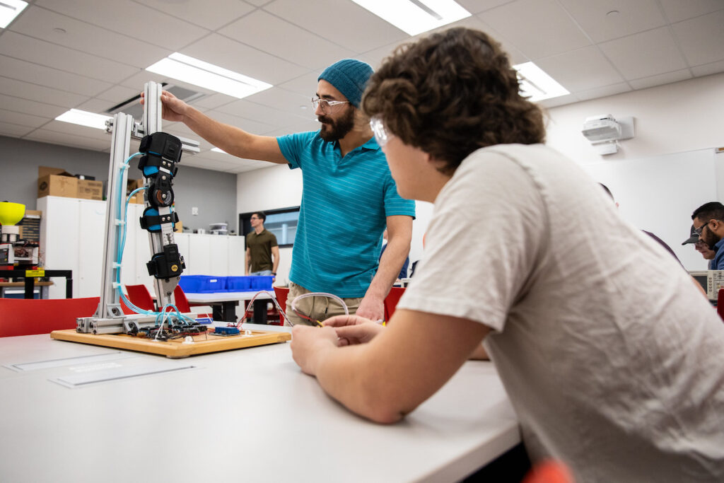Two students working on a robotic arm in a mechatronics lab.