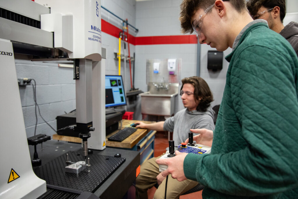 Three students using a coordinate measuring machine in a shop environment.