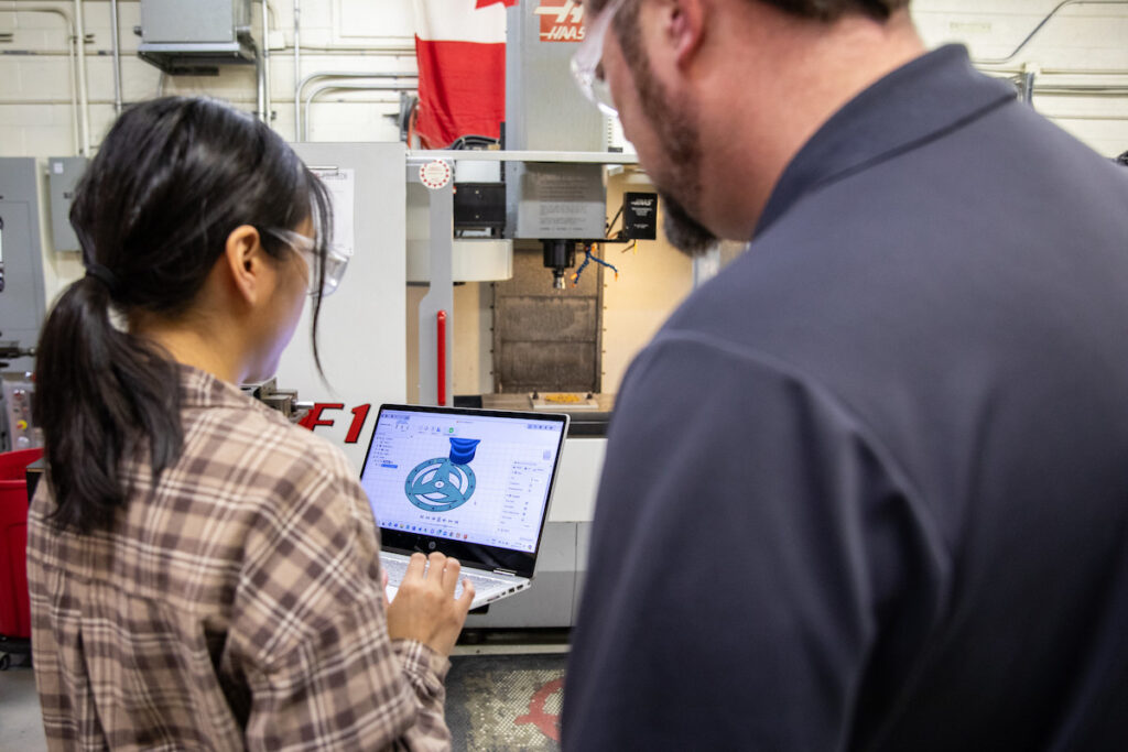 Student and instructor looking at 3D design software in front of a CNC machine.
