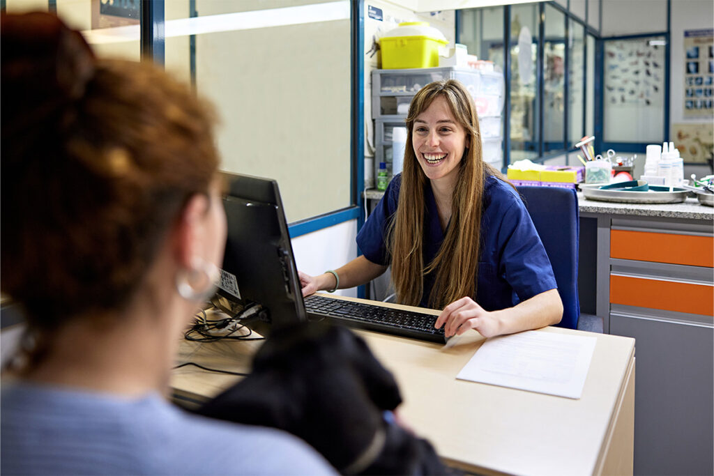 Woman on a computer smiling and talking to somebody across the table