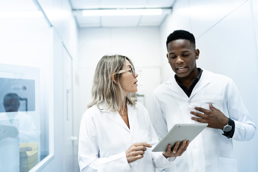 Two people in white coats in a medical setting looking at a tablet