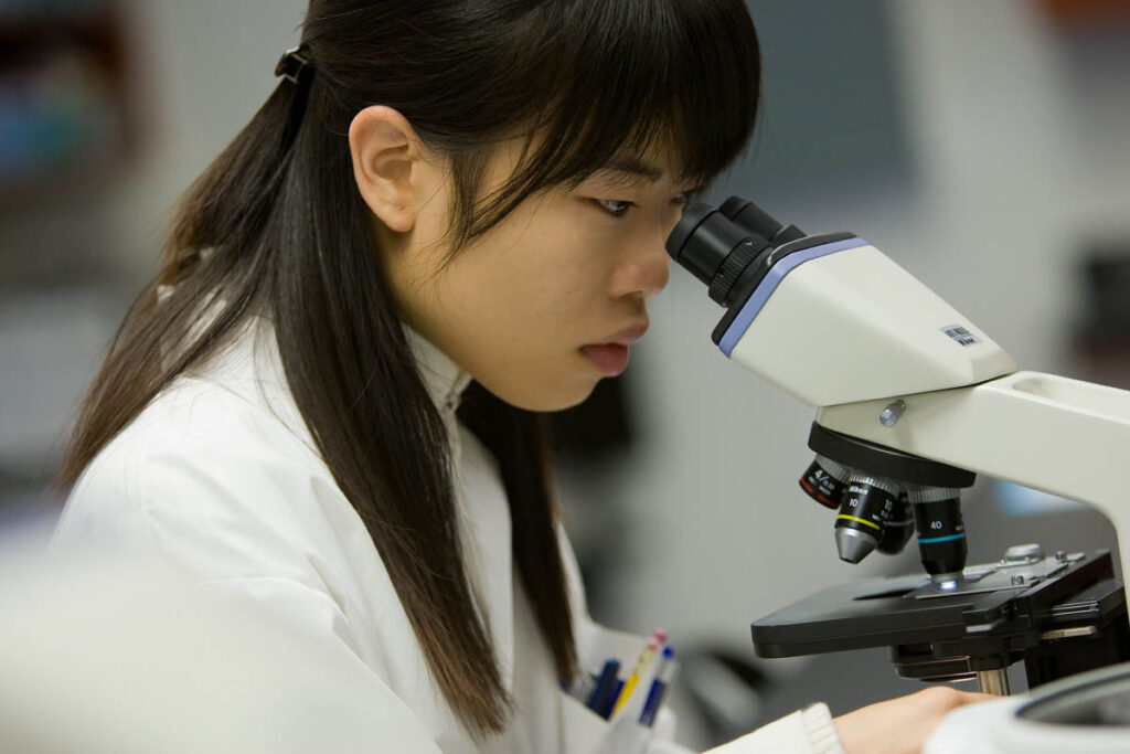 Student wearing a lab coat and looking into microscope
