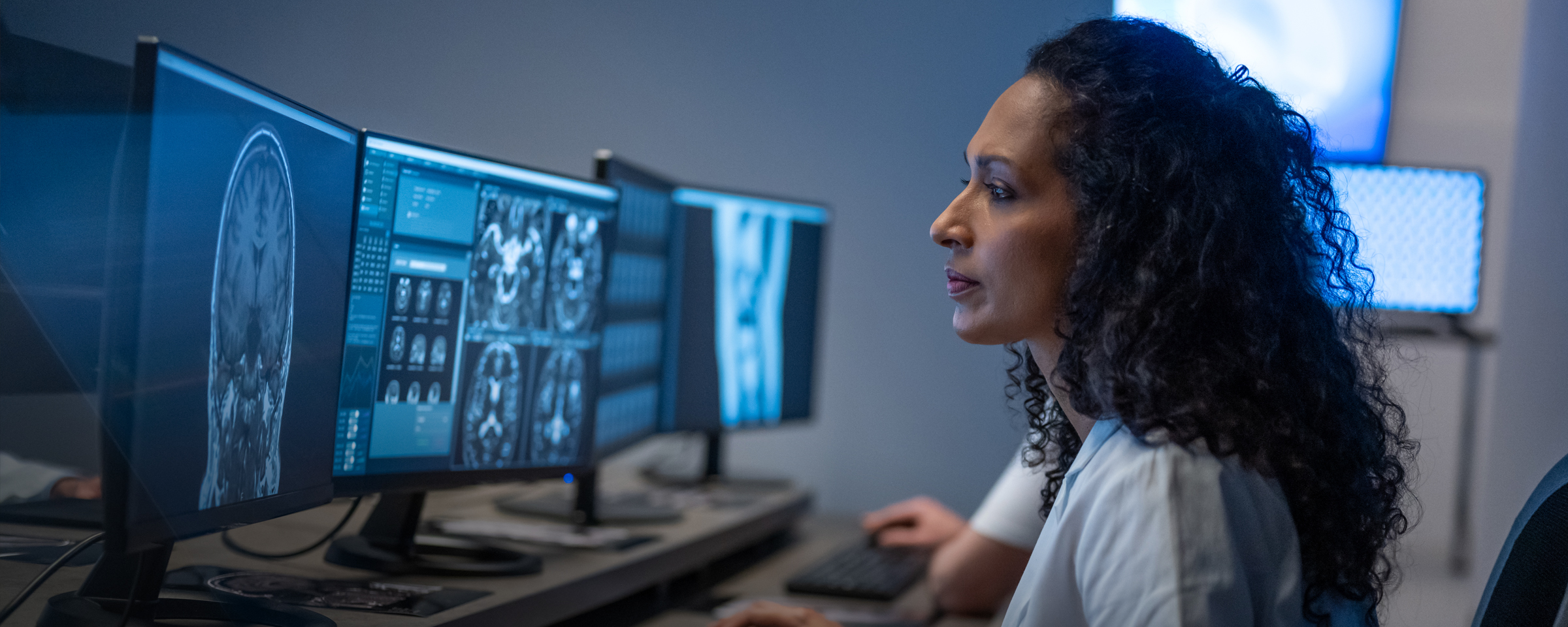 Woman sitting in front of three monitors in a dark room looking at MRI scans