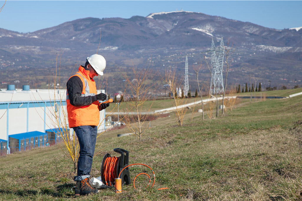 Engineer wearing an orange safety vest standing on a hill overlooking some power lines