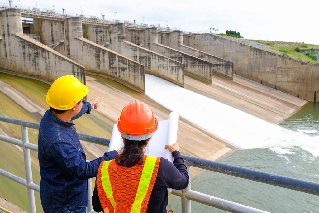 Two engineers with blueprints looking over a dam