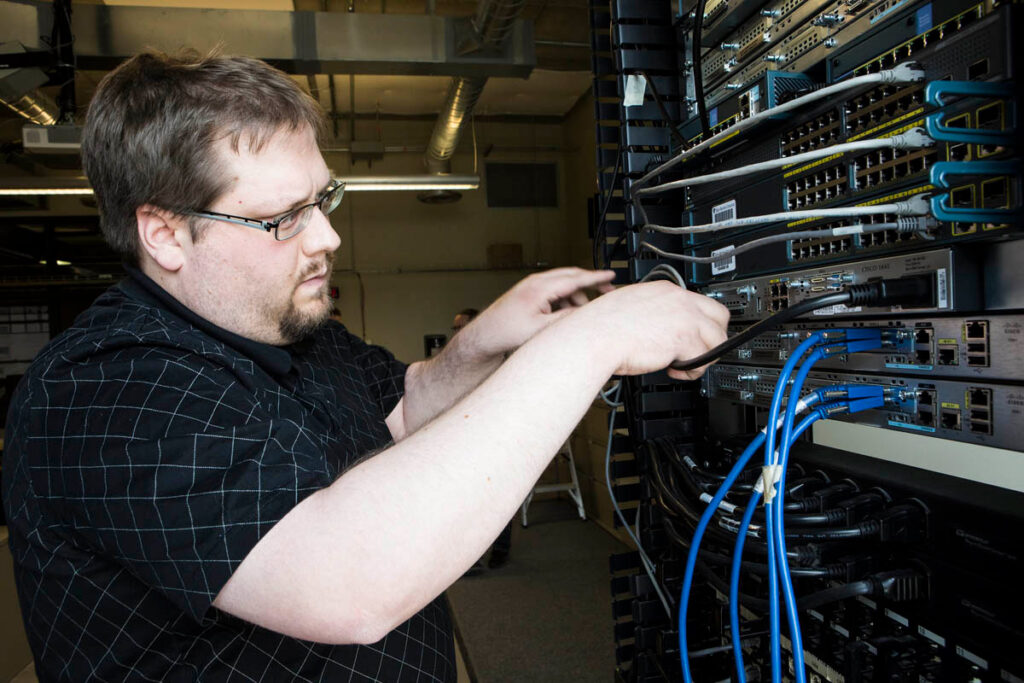 Student plugging cables into networking switches in lab