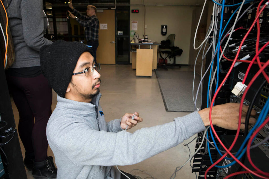 Student plugging cables into networking switches in lab