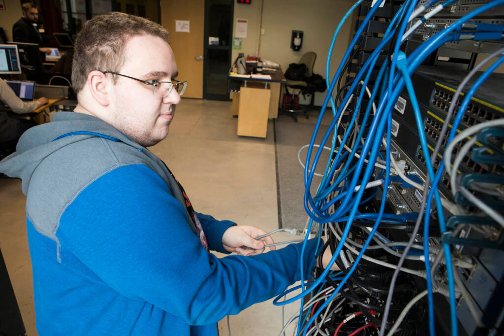 Student plugging cables into networking switches in lab