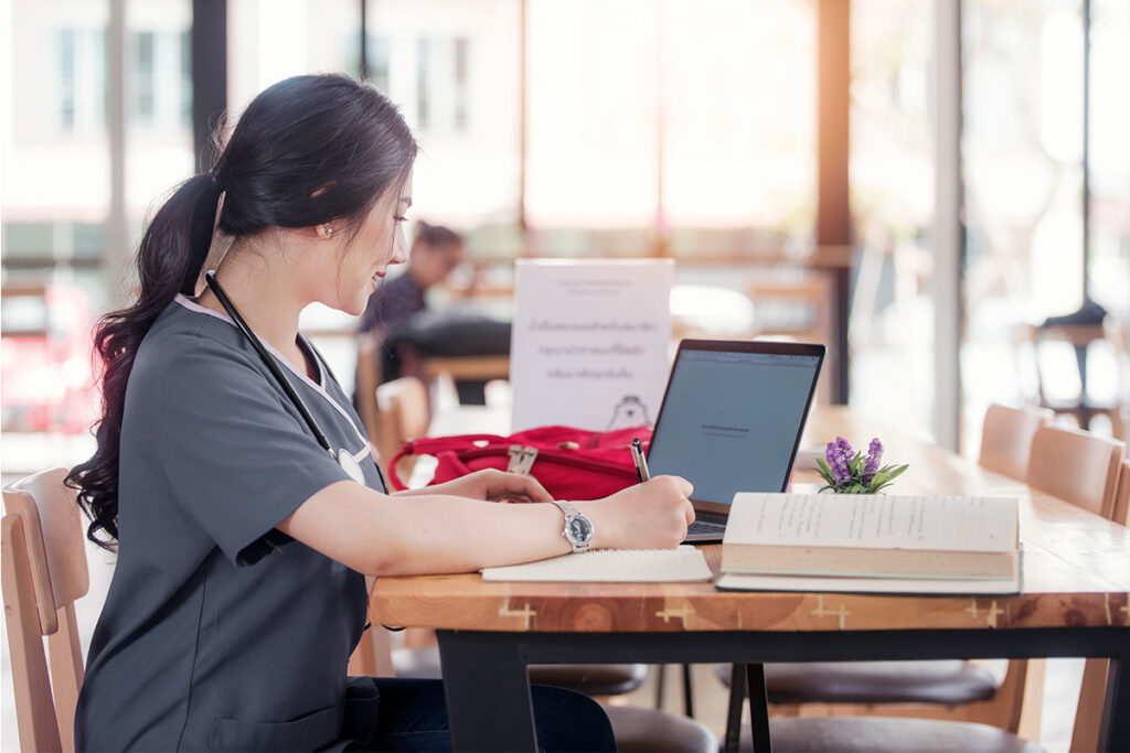 Nurse sitting at a table with a laptop and taking notes