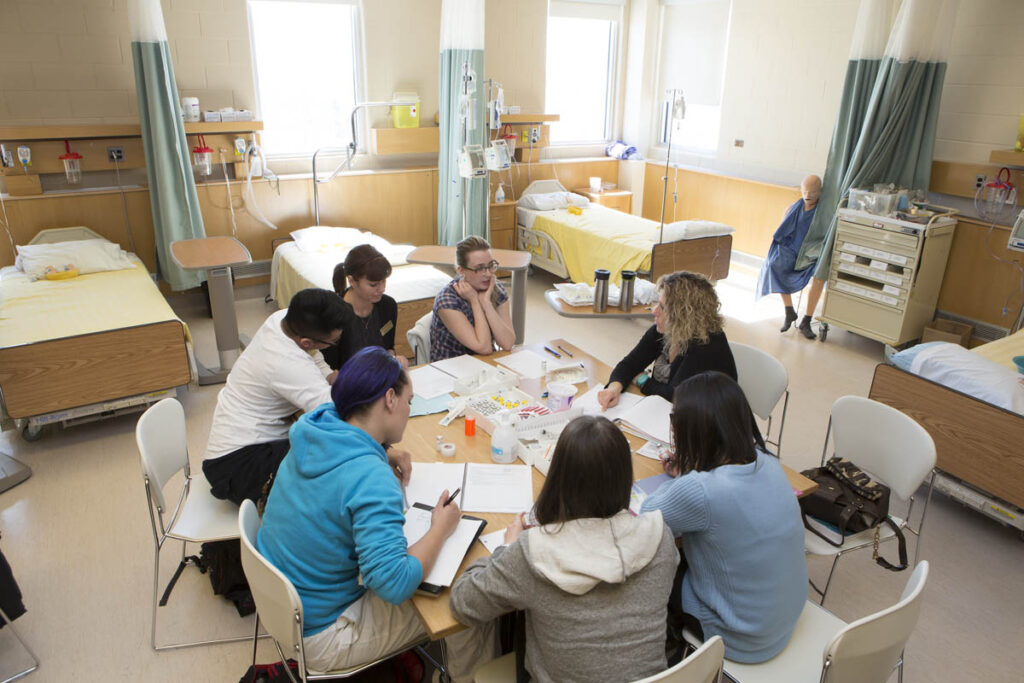 Instructor and students sitting around a table in a hospital training lab