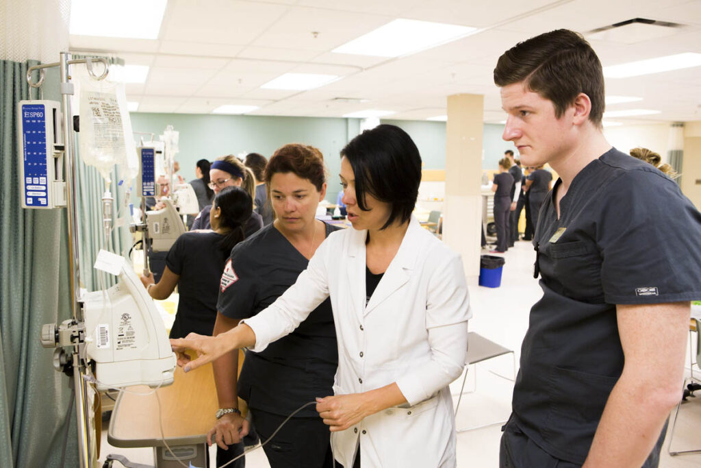 Nursing instructor showing students how to use equipment in a simulated hospital room
