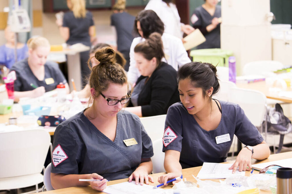 Nursing students sitting at a table and taking notes in a nursing lab