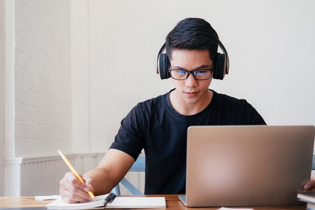 Guy wearing headphones sitting at a table and taking notes