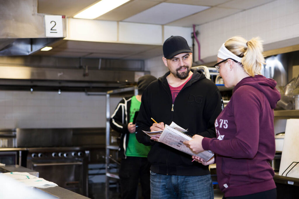 Two people taking notes on a clipboard in an industrial kitchen 