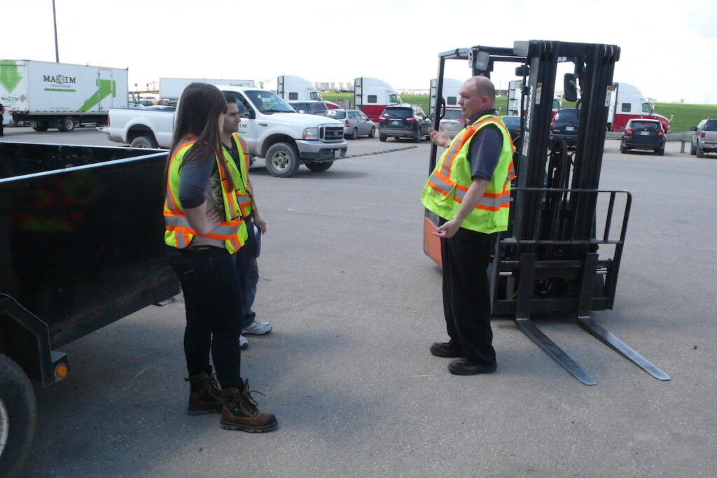 Three people in safety vests standing outside by forklift 