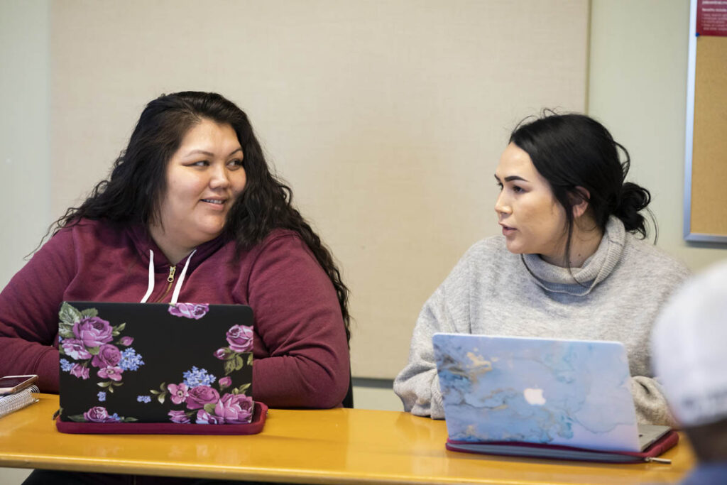 Two women on laptops in a classroom