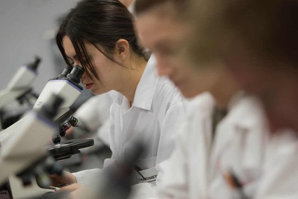 Student in white coat looking at something through a microscope