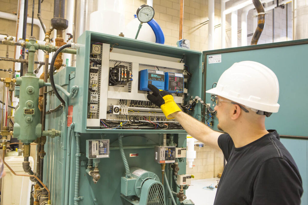 Power engineer in hard hat working with on a control panel