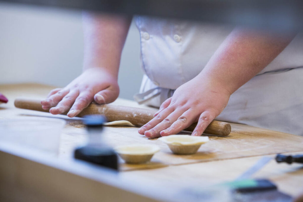 Baker using rolling pin to flatten dough