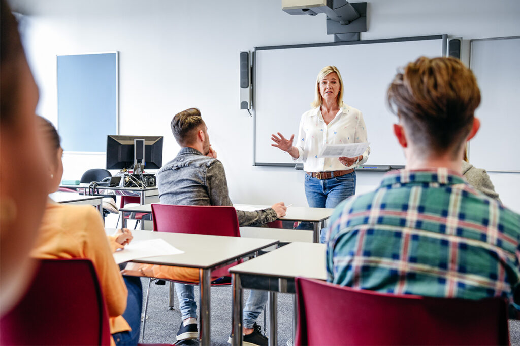 Instructor standing at the front of a classroom talking to her class