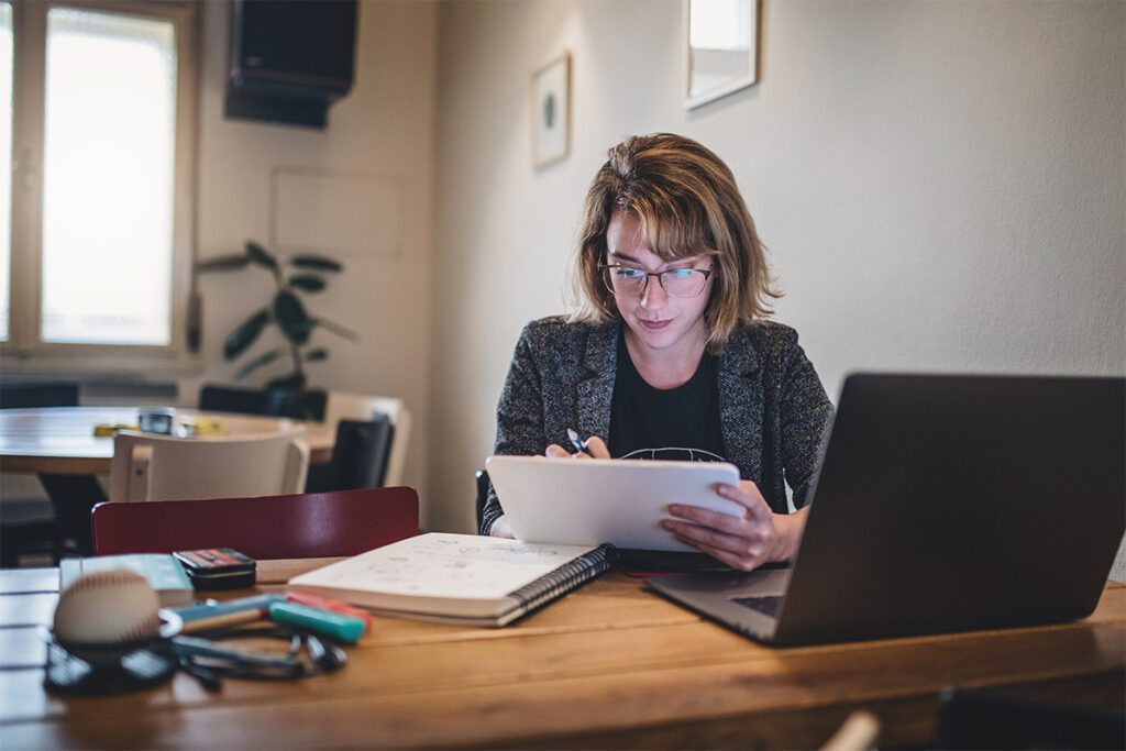 Woman sitting at a table with a laptop while doing something on her tablet