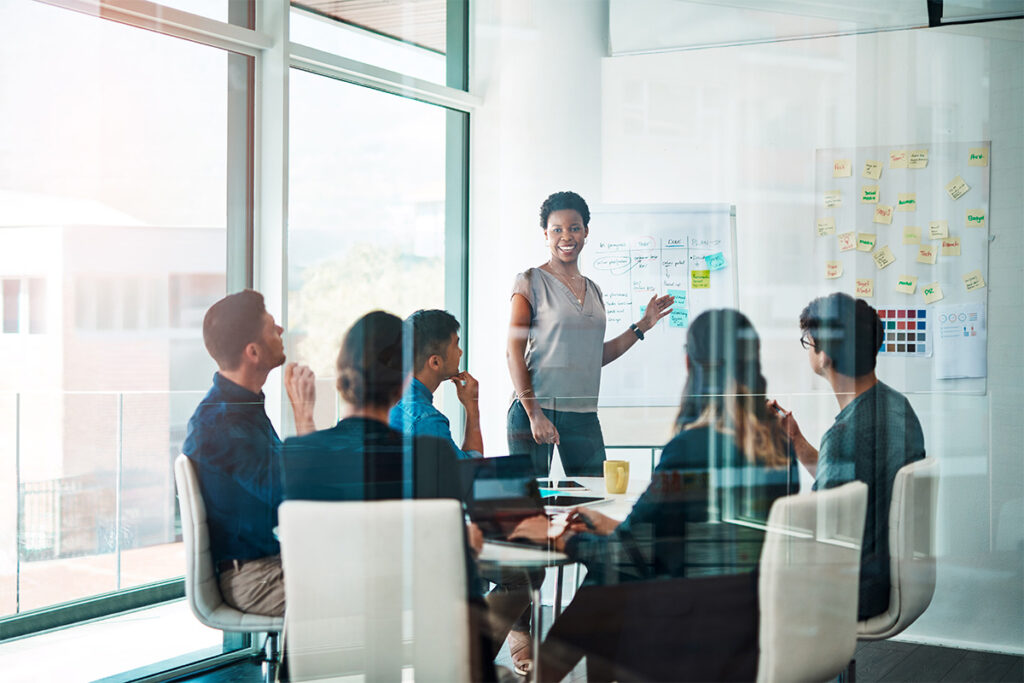 Woman giving a presentation to her colleagues in a glass meeting room