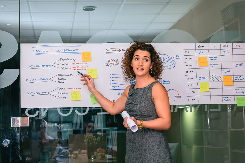 Woman giving a presentation and is pointing at information on a whiteboard