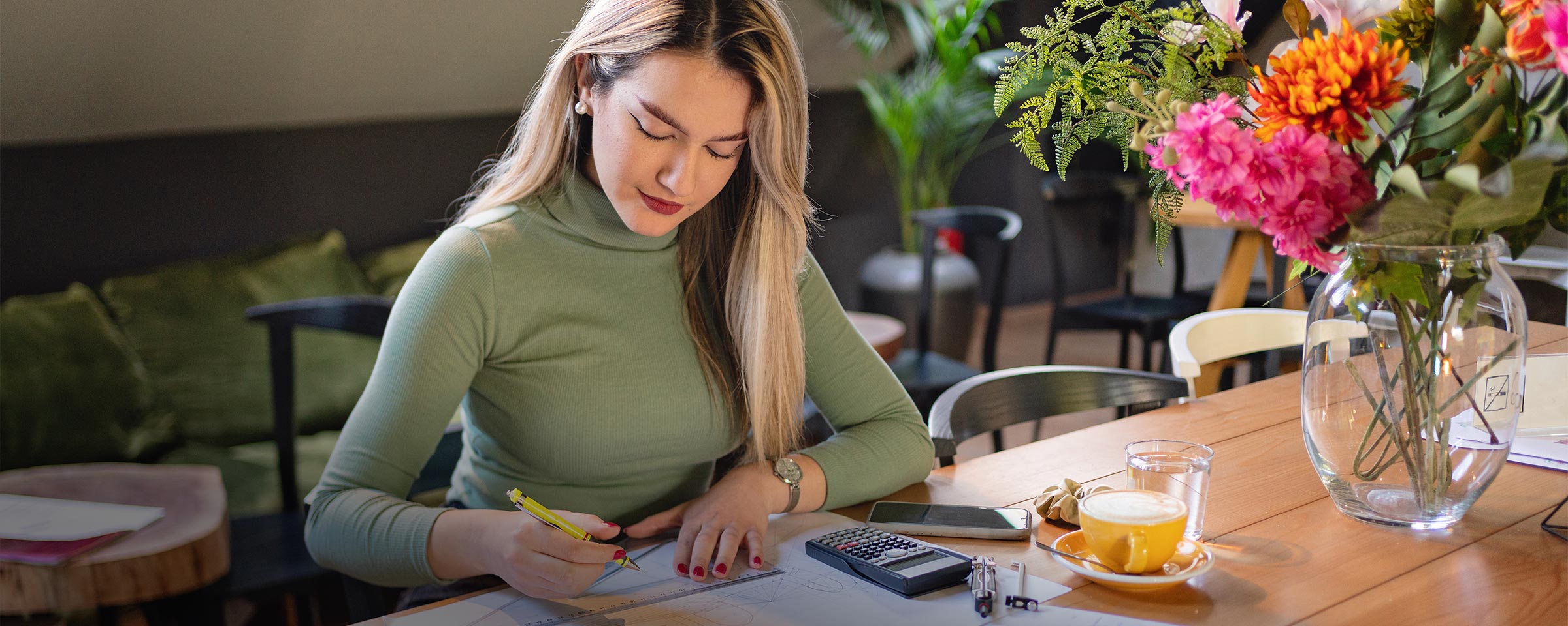 Woman sitting in a restaurant with flowers on the table and is drawing a floor plan