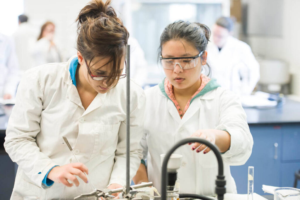 Students wearing white lab coats taking notes in a science laboratory