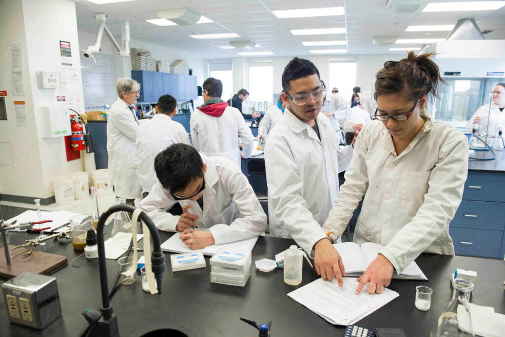 Students wearing white lab coats taking notes in a science laboratory