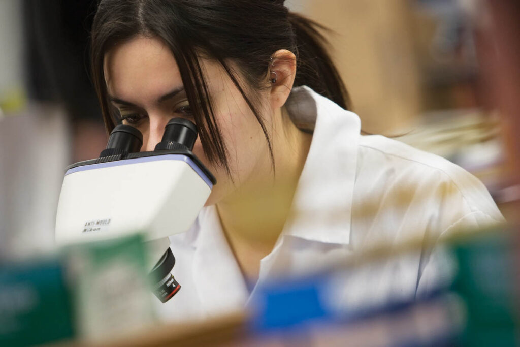 Student wearing lab coat and looking through microscope