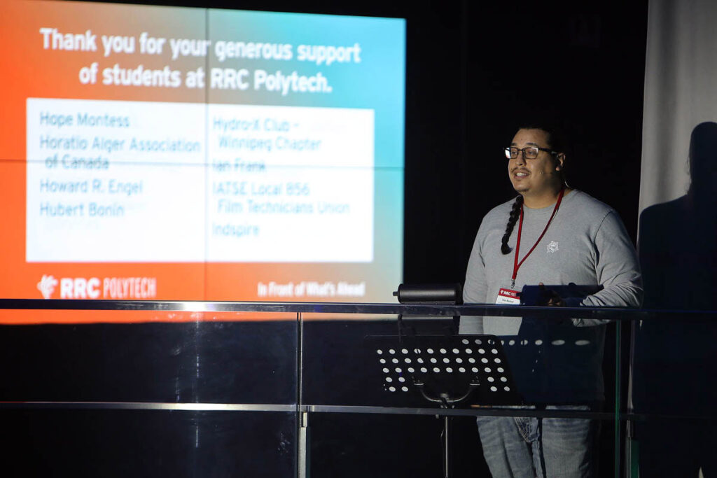 Person on stage giving a speech next to projector screen