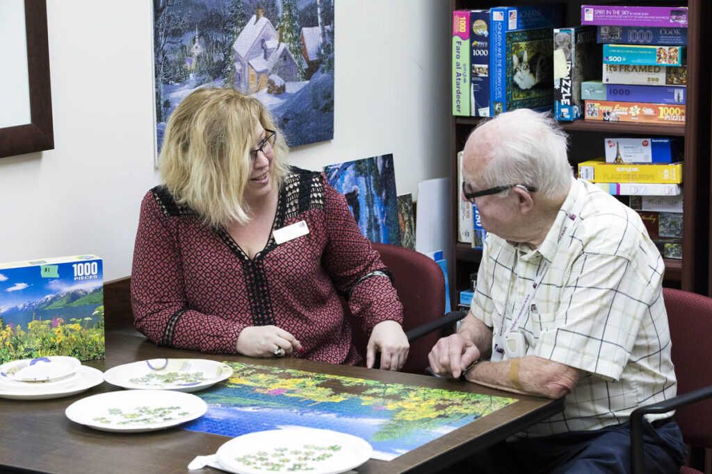 Woman sitting by elderly man who just completed a puzzle at a care home