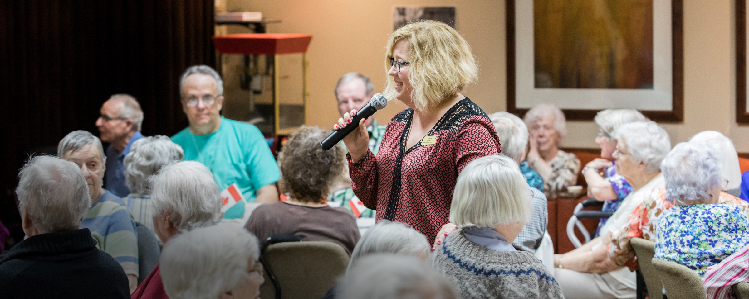 Woman standing up and talking to a group of older adults in a care home setting