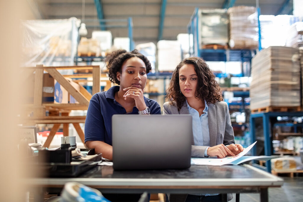 Two people looking at a laptop and talking in a warehouse