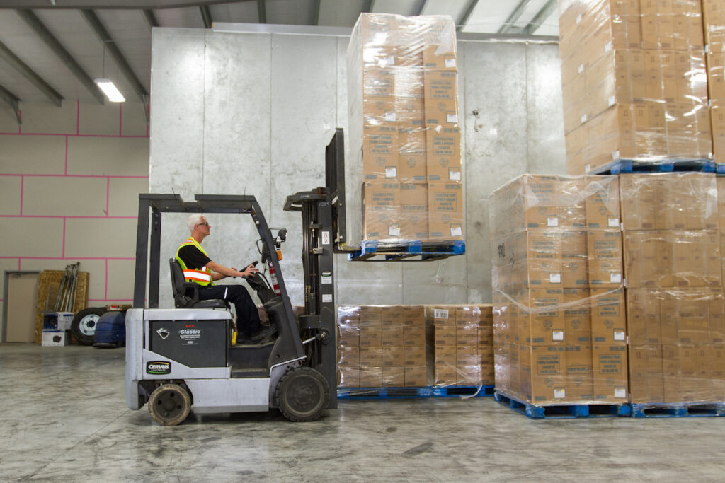 Forklift operator lifting palettes of boxes in a warehouse