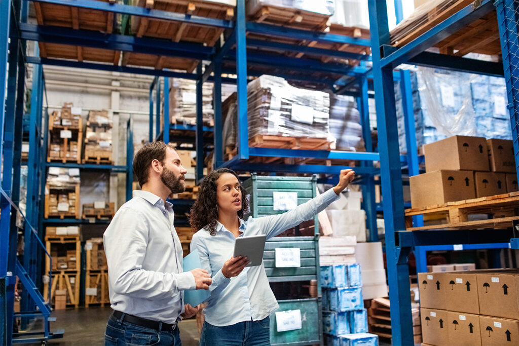 Two people talking and looking at boxes in a large warehouse