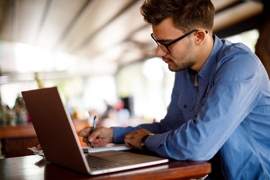 Man working on a laptop and taking notes