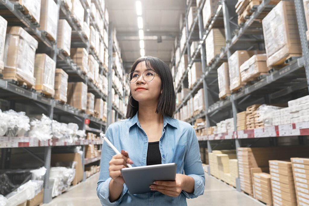 Woman walking through a large warehouse and taking notes on a tablet