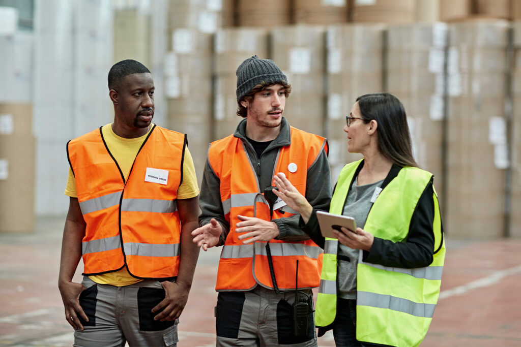 Three people in safety vests talking in a warehouse