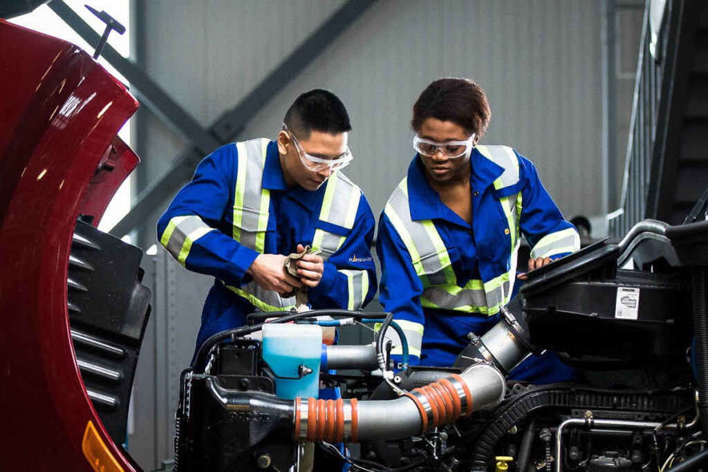 Two people working under the hood of a vehicle