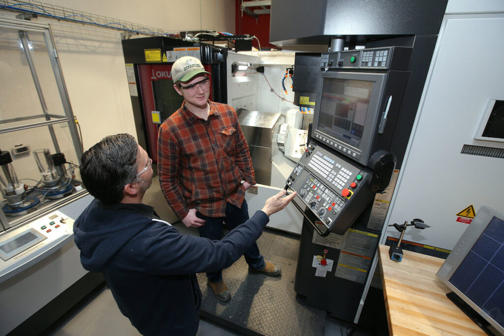 Instructor and student standing by manufacturing device