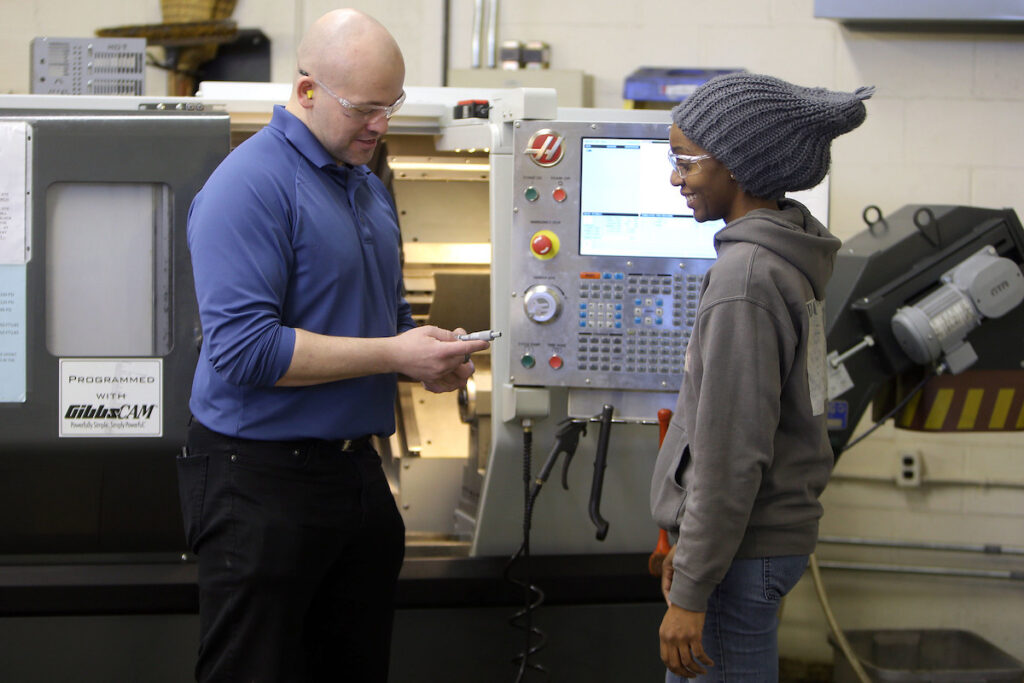 Instructor and student standing by manufacturing device