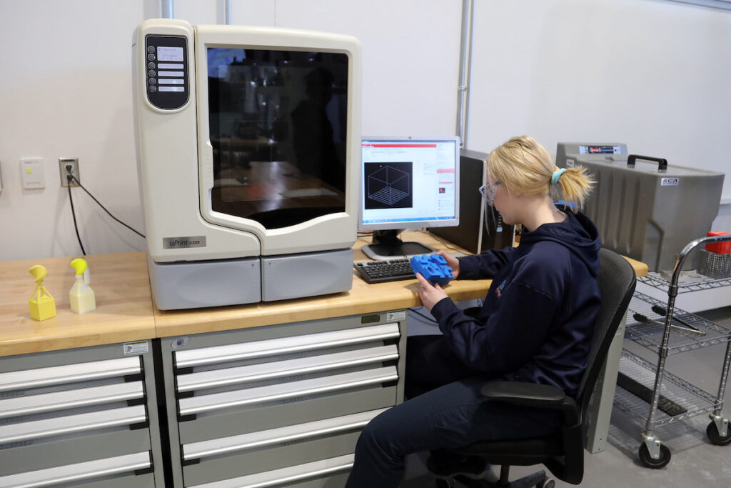 Student working on computer next to manufacturing machine