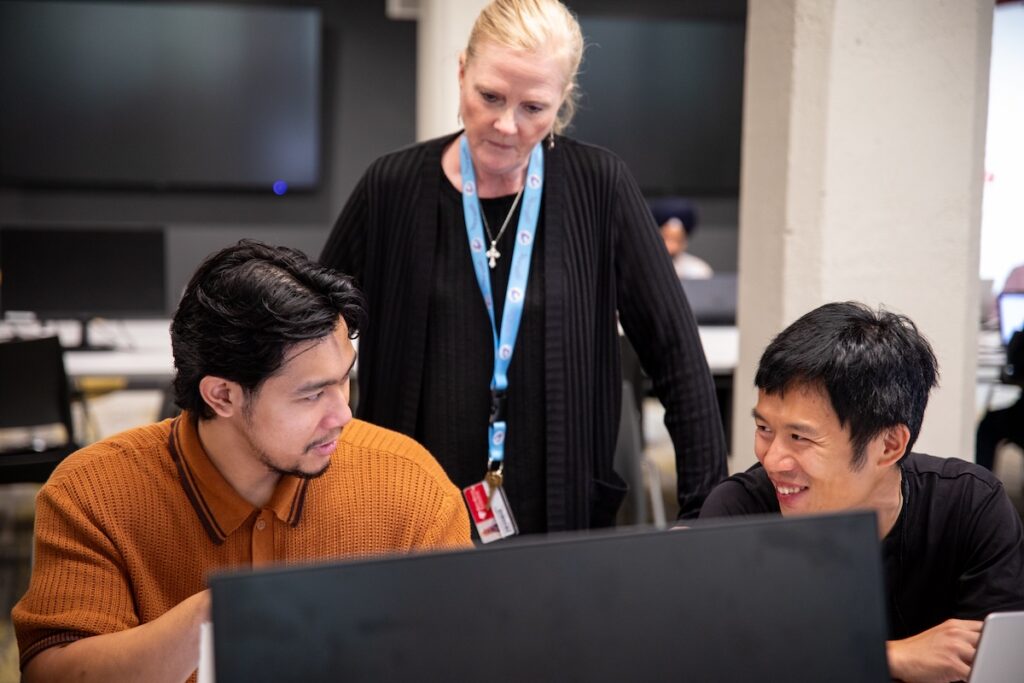 Two students and one instructor interacting at a computer lab
